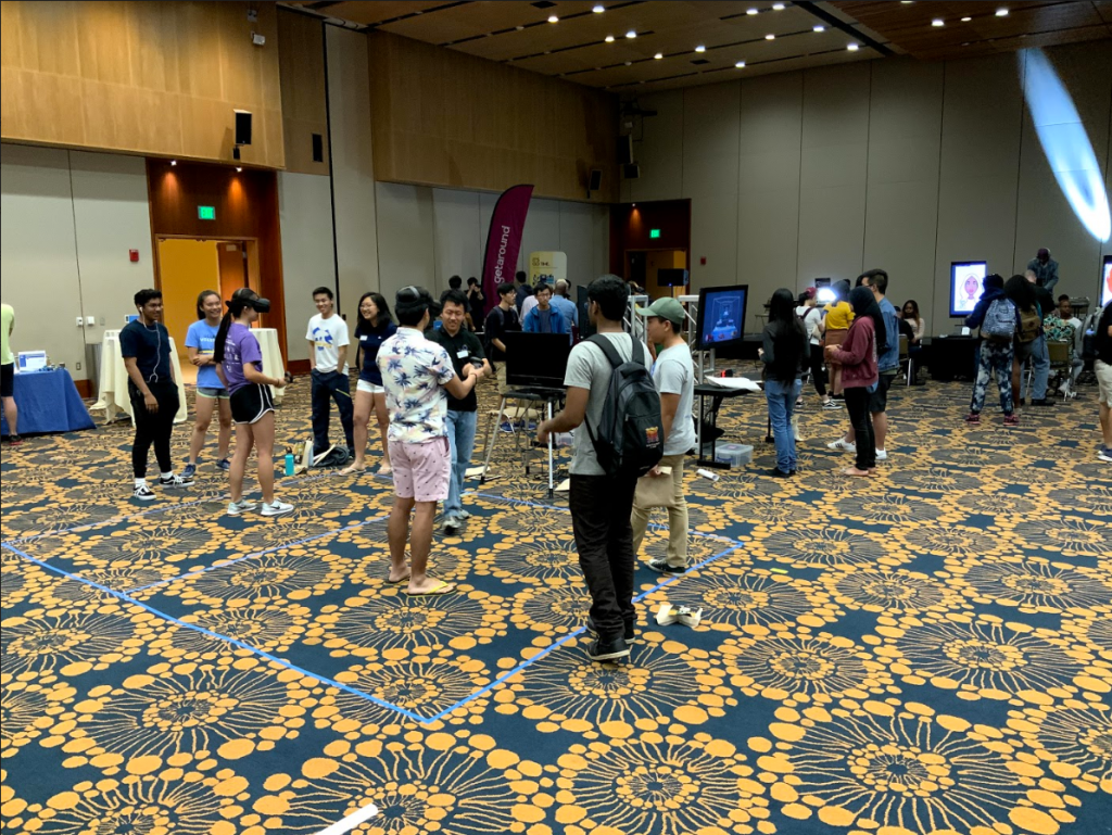 A crowd of students gather around two virtual reality headset demoes